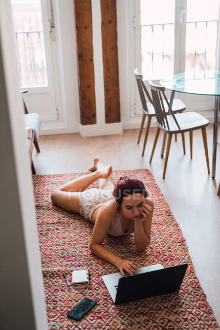 Jeune femme couchée sur le sol à la maison et utilisant un ordinateur portable — Photo de stock
