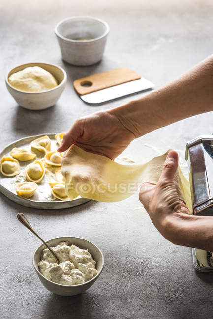 Mains humaines préparant tortellini avec fromage cottage sur plateau gris — Photo de stock
