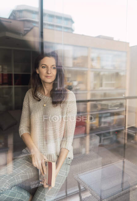 Adult woman with book standing close to sofa and window — Stock Photo