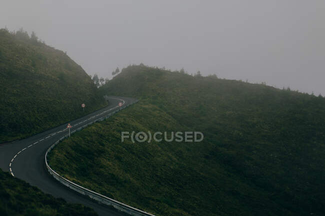 Leere Autobahn auf grünem Hügel vor grauem Himmel — Stockfoto