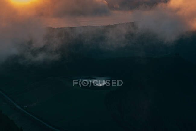 Vista aérea do lago azul pequeno no campo vasto verde com névoa grossa acima — Fotografia de Stock