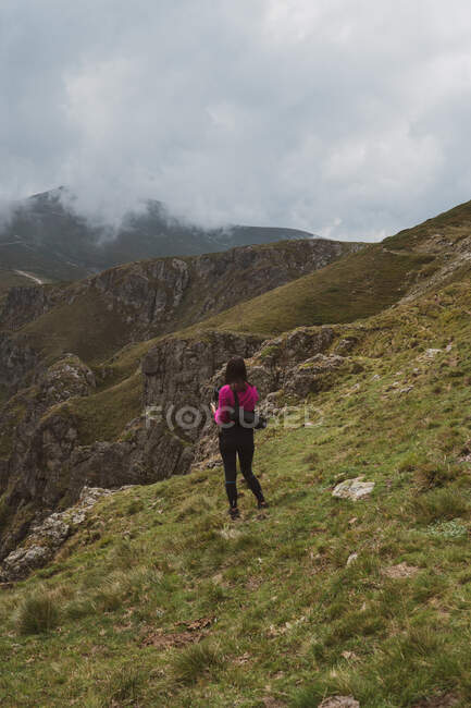 Назад вид молодой женщины в повседневной одежде, стоящей на вершине травянистой горы и любуясь захватывающим видом на красивую природу в облачный день в Болгарии, на Балканах — стоковое фото