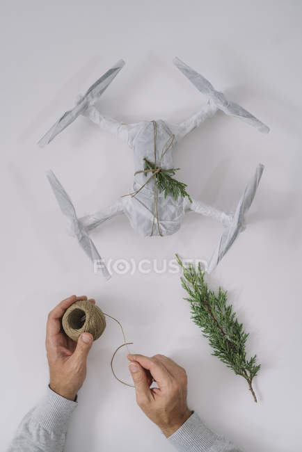 Mãos masculinas decorando drone envolto como presente de Natal com ramo de abeto e cordel no fundo branco — Fotografia de Stock