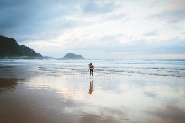 Visão traseira da jovem mulher em pé na areia molhada da praia perto do mar ondulando no dia nublado em Zarautz, Espanha — Fotografia de Stock