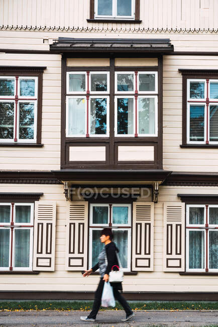 Vue latérale de la femelle avec sac marchant sur la chaussée près de la vieille maison étonnante sur la rue de la petite ville — Photo de stock