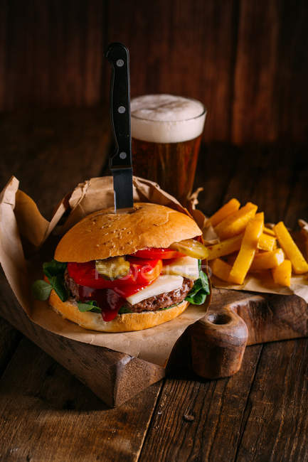 Delicious gourmet burger with knife on plate on dark wooden background with beer and fries — Stock Photo