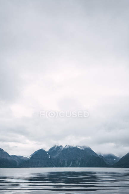 Eaux tranquilles du lac et montagnes rocheuses sous un ciel nuageux, Laponie — Photo de stock