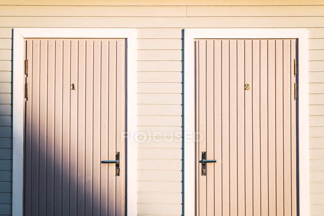 Two doors with numbers on facade of wooden light pink residential building — Stock Photo