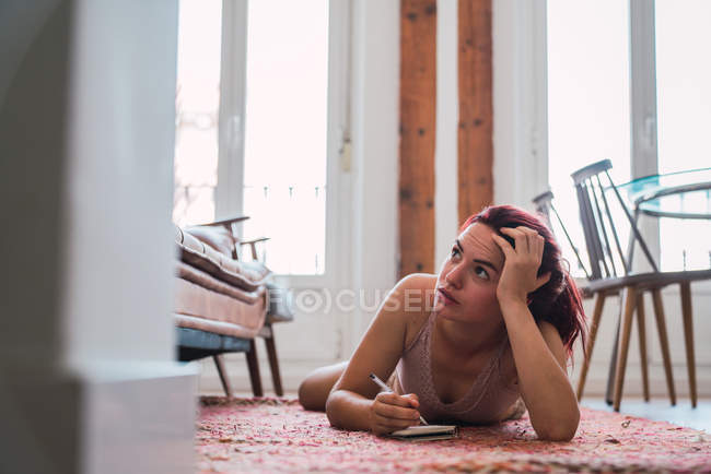 Жінка в нижній білизні лежить на підлозі і пише в блокноті — стокове фото