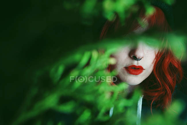 Young red haired woman between fir twigs on black background — Stock Photo