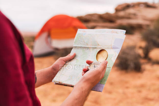 Crop man sosteniendo mapa y brújula retro mientras está de pie sobre un fondo borroso del majestuoso desierto - foto de stock