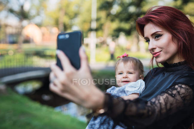 Jovem mãe elegante tomando selfie com bebê alegre no parque — Fotografia de Stock