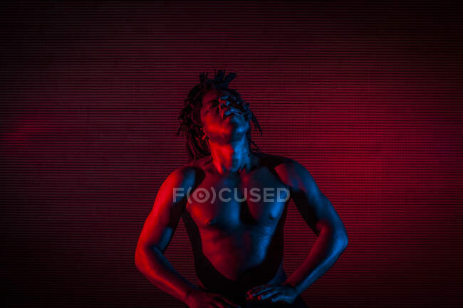 Junger afrikanischer rastafarian mann probt gerne und spielt tam tam, farbige beleuchtung rot und blau — Stockfoto