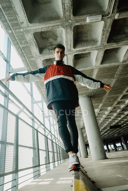 Junger gutaussehender Mann in Sportjacke läuft auf Eisenschiene in geräumigem Gebäude mit Säulen — Stockfoto
