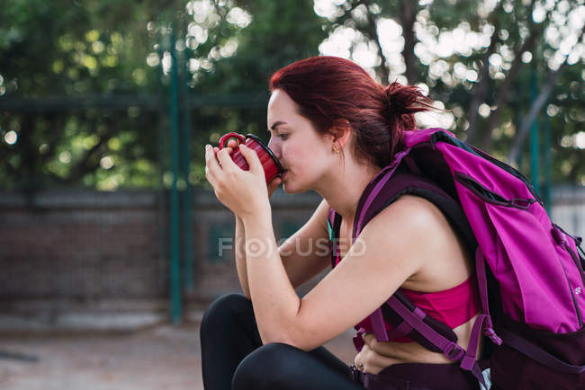 Junge Sportlerin mit Rucksack sitzt draußen und trinkt Kaffee — Stockfoto