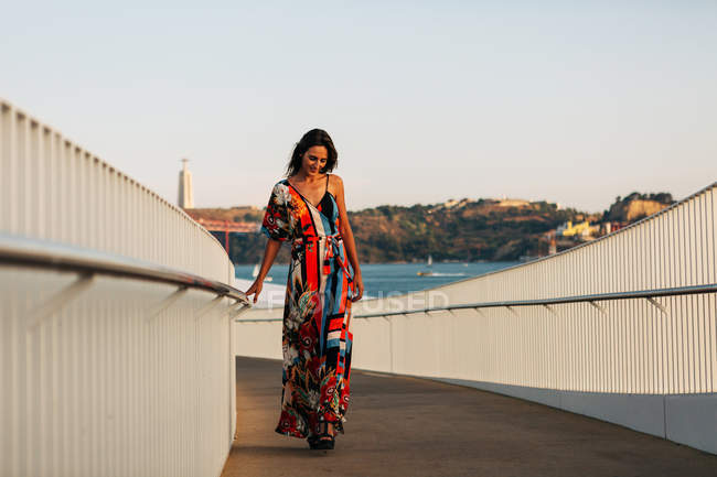 Mujer elegante en vestido largo caminando en el puente en la ciudad de verano - foto de stock