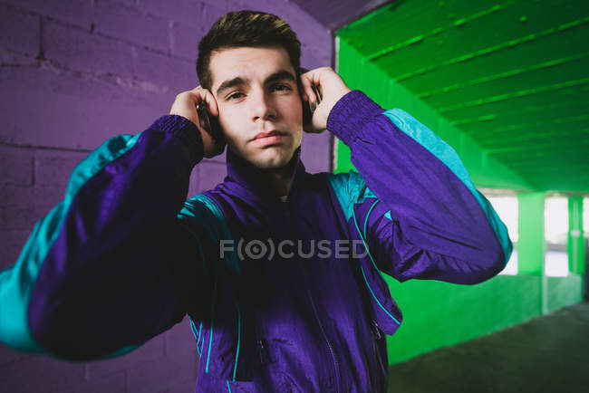 Retrato de hombre joven en ropa deportiva escuchando música contra la pared colorida - foto de stock