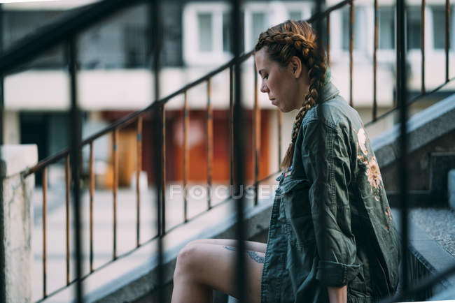Pensive red-haired girl with braids sitting on staircase in city — Stock Photo
