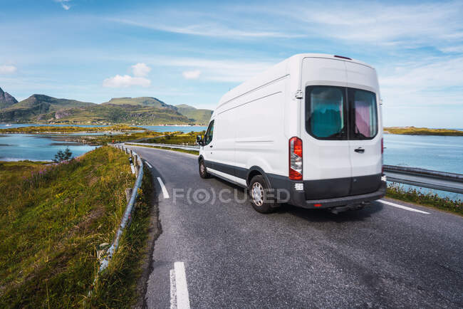 White bus driving on asphalt motorway on background of blue still river and mountains under clear sky — Stock Photo