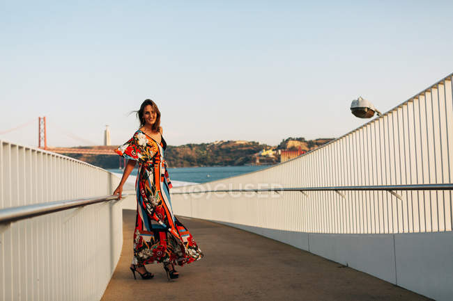 Элегантная женщина в длинном платье прогулка по мосту в летнем городе — стоковое фото