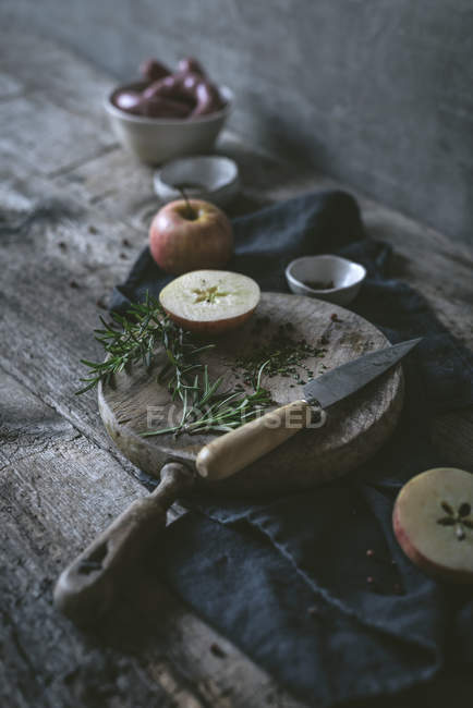Romero fresco y cuchillo afilado en mesa de madera cerca de manzana madura - foto de stock
