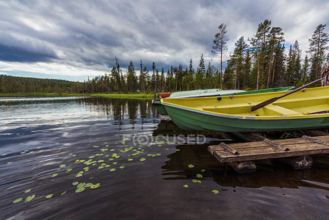 Barche gialle e verdi ormeggiate sulla riva del fiume increspato sullo sfondo di montagne e cielo nuvoloso — Foto stock