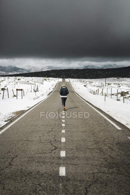 Vista posteriore del giovane in abito elegante a piedi in mezzo alla strada asfaltata sulla giornata invernale nuvolosa nella splendida campagna — Foto stock