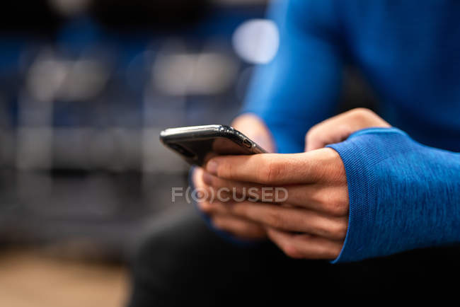 Mãos de homem em pulôver azul usando smartphone em fundo borrado — Fotografia de Stock