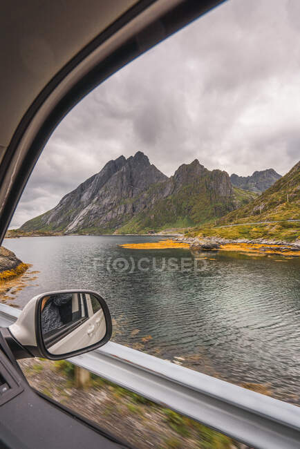 Landscape of high beautiful mountains near rippling river under cloudy sky through window of moving car — Stock Photo
