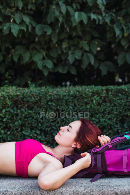 Sportswoman lying on stone bench in park with backpack — Stock Photo