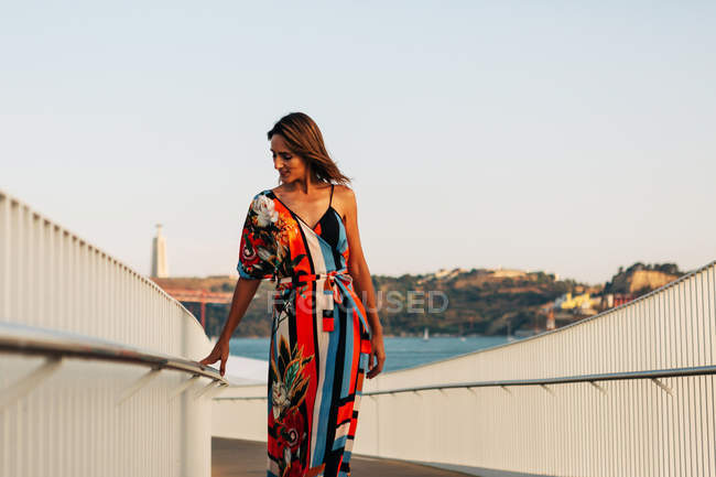 Mujer elegante en vestido largo caminando en el puente en la ciudad de verano - foto de stock