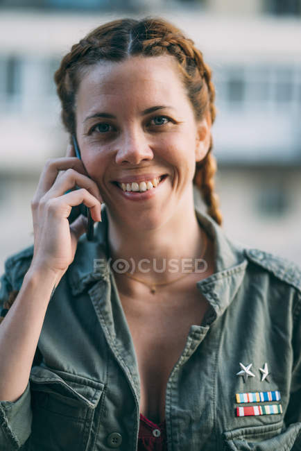 Портрет рыжеволосой молодой женщины с косичками, разговаривающей по мобильному телефону на улице — стоковое фото