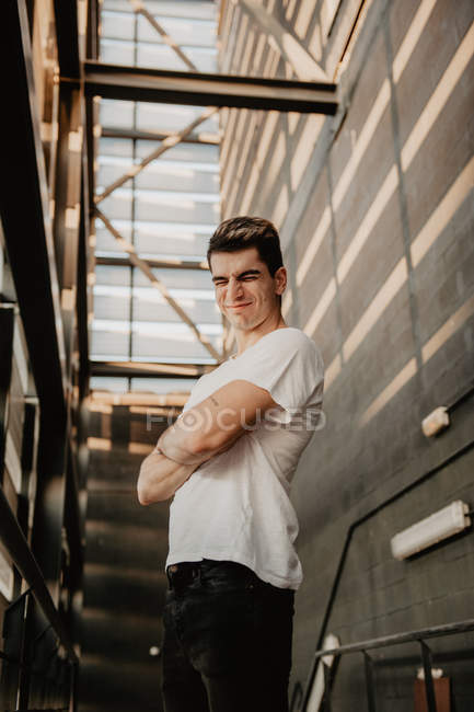Cheerful young man standing and squinting on stairs in building — Stock Photo