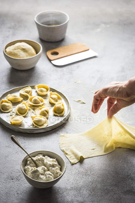Human hand preparing tortellini with cottage cheese on grey tabletop — Stock Photo