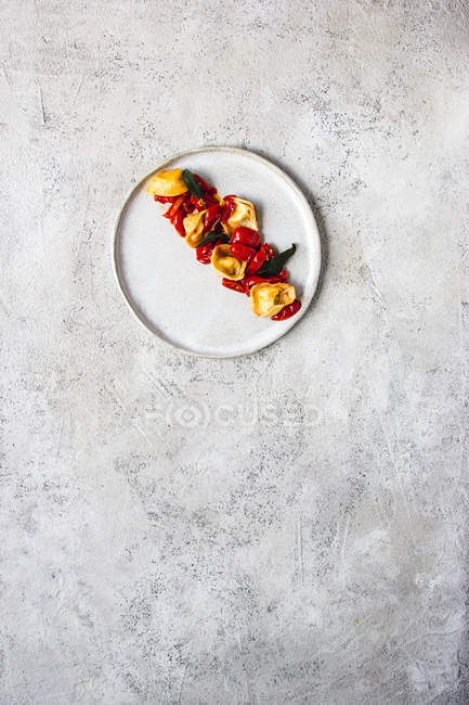 Delicioso prato de tortellini com tomate servido em prato em mesa cinza — Fotografia de Stock