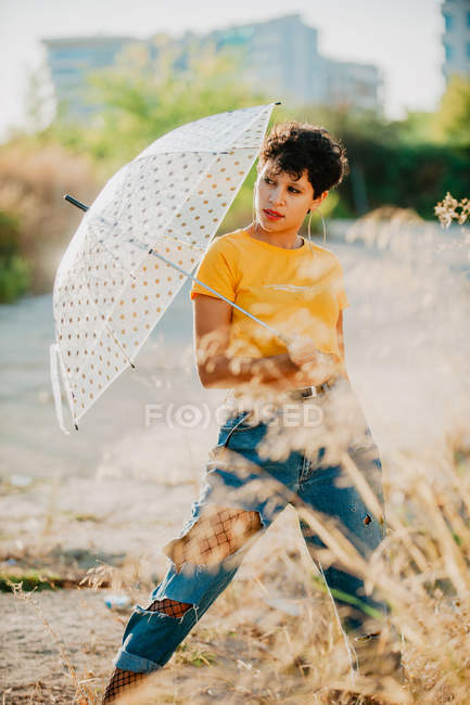 Jeune femme réfléchie avec parapluie debout à l'extérieur et regardant loin — Photo de stock