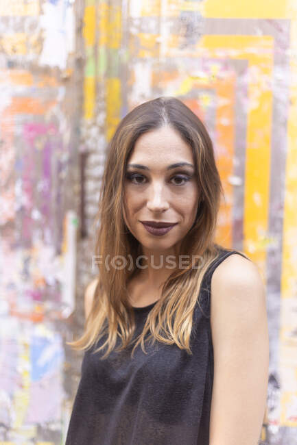 Attractive female with stylish makeup looking at camera while standing near colorful wall on city street — Stock Photo