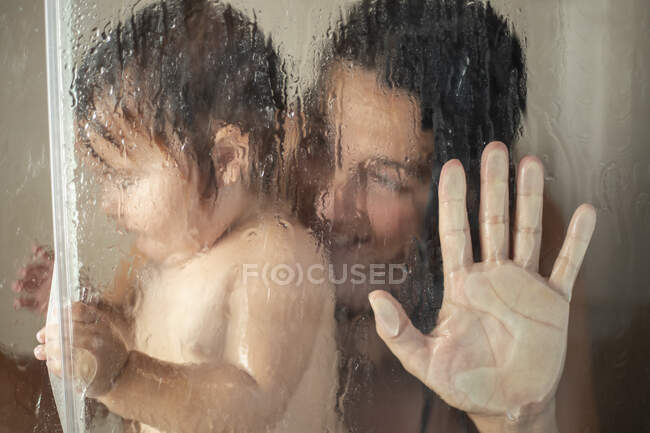 Tiro através de vidro stall de mulher tomando banho com criança e sorrindo — Fotografia de Stock