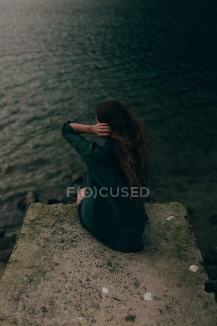 Jeune femme assise sur une falaise près du lac — Photo de stock