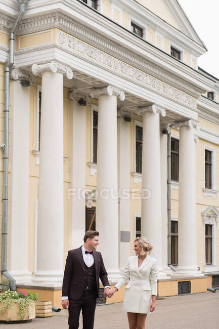 Dal basso di bella donna e uomo che indossano abiti da sposa eleganti e si sorridono a vicenda sullo sfondo di un vecchio edificio — Foto stock