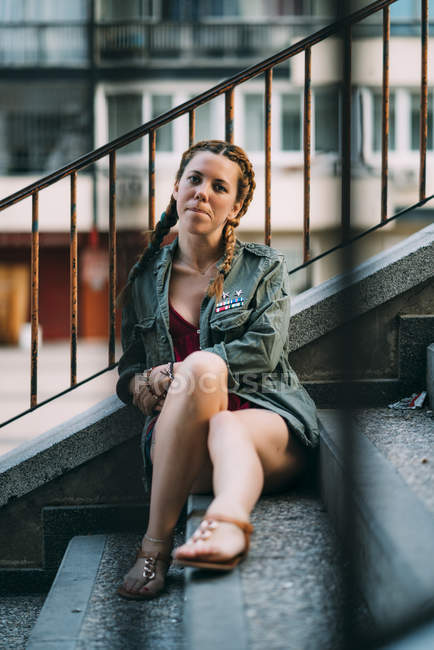 Вдумлива руда дівчина з косами, що сидить на сходах міста — стокове фото