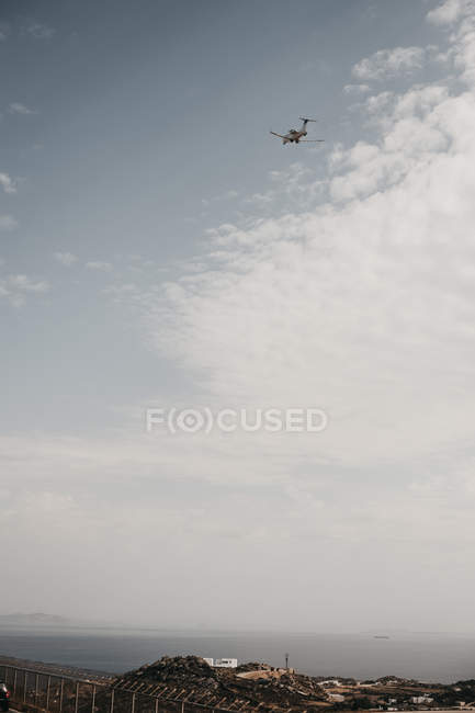 From below view of white aircraft flying in cloudy sky over sea in Mykonos, Greece — Stock Photo