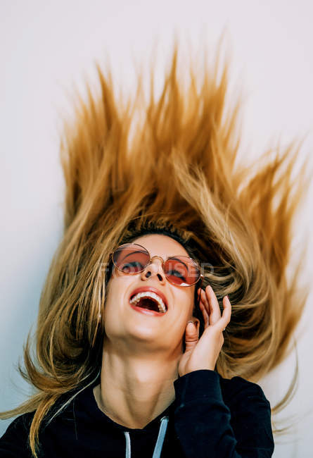 Giovane donna bionda in pullover nero e occhiali da sole con capelli lunghi biondi che ballano su sfondo bianco — Foto stock