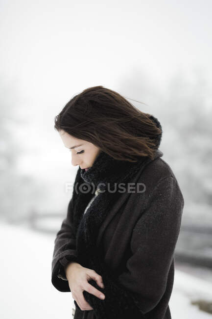 Вид сбоку на молодую женщину в теплой одежде, идущую рядом с забором в ветреный зимний день в великолепной сельской местности — стоковое фото