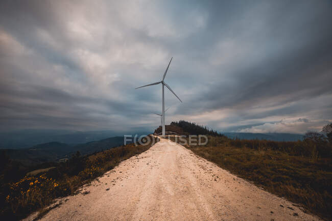 Fila di mulini a vento moderni in piedi sul lato della stretta strada di campagna nelle giornate nuvolose — Foto stock
