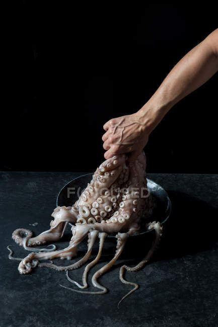 Menschliche Hand hält Oktopus über Teller auf schwarzem Marmorhintergrund — Stockfoto