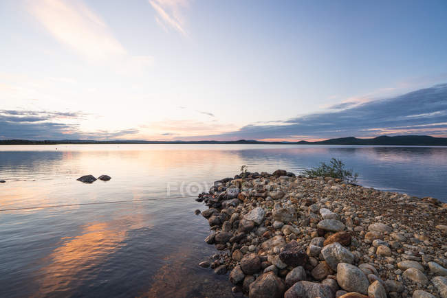 Superficie del tranquillo lago blu con cielo nuvoloso al tramonto, Lapponia — Foto stock
