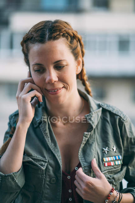 Retrato de mujer joven pelirroja con trenzas hablando en el teléfono móvil al aire libre - foto de stock