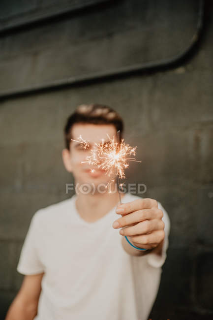Young handsome man in white T-shirt standing inside building and holding burning Bengal light in hand — Stock Photo