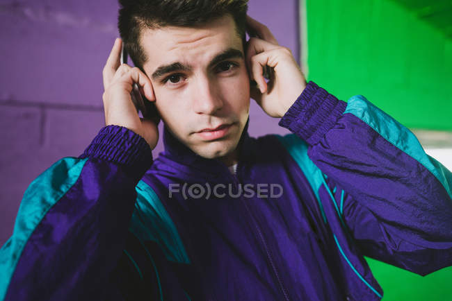 Portrait de jeune homme en tenue de sport écoutant de la musique contre un mur coloré — Photo de stock
